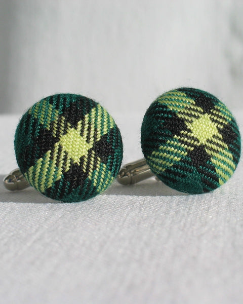 Green and black plaid patterned cufflinks on a textured white background