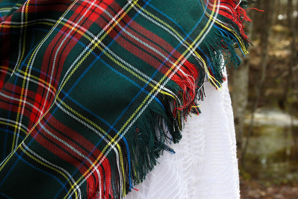 close up of Green Stewart tartan blanket scarf fringe with trees in the background