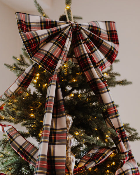 close up of dress stewart tartan white red green and gold plaid christmas tree bow on the top of a christmas tree.