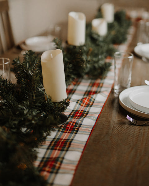 Dress Stewart tartan table runner on a wooden table tpped with greenry and white candles.
