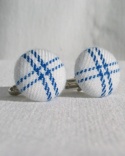 White cufflinks with blue pattern on a light gray background