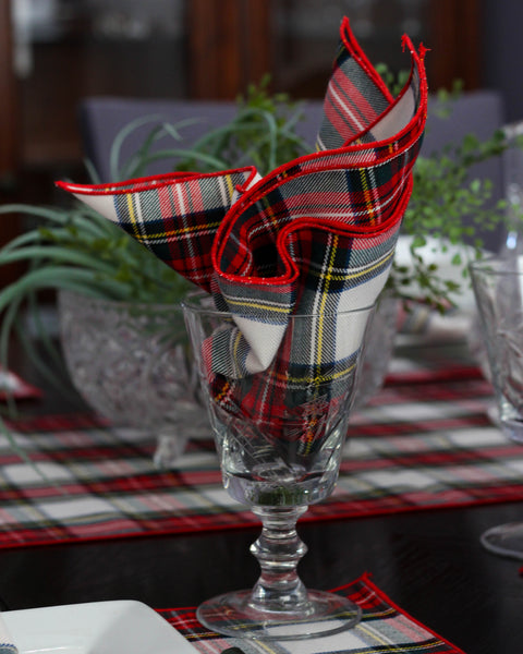White Plaid napkin folded into a decorative shape on a glass with a table setting in the background.