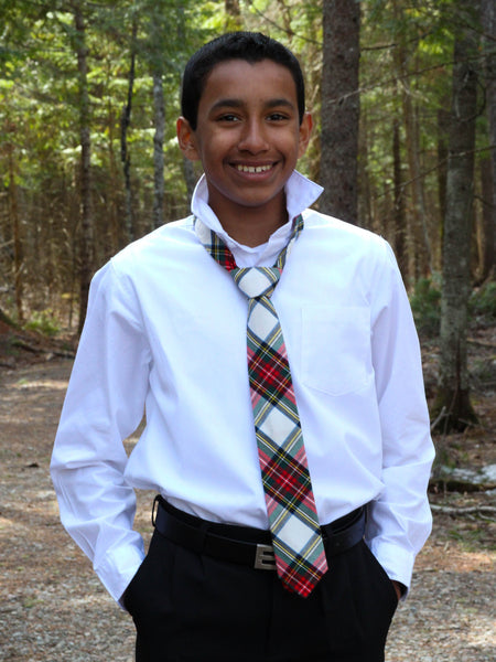 Young boy wearing a white shirt and plaid tie in a forest setting