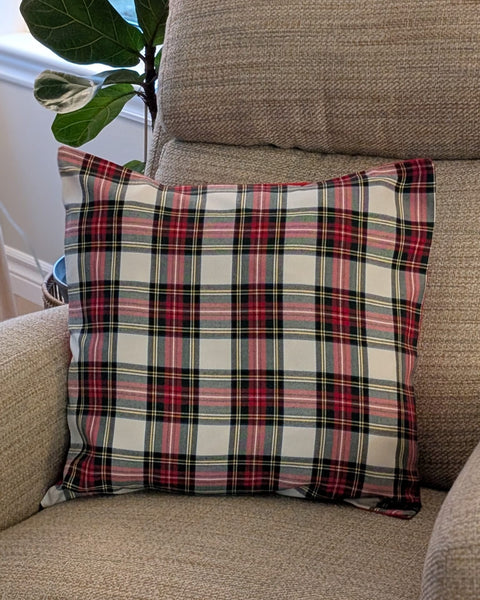 White and red plaid pillow on a beige sofa with a plant in the background