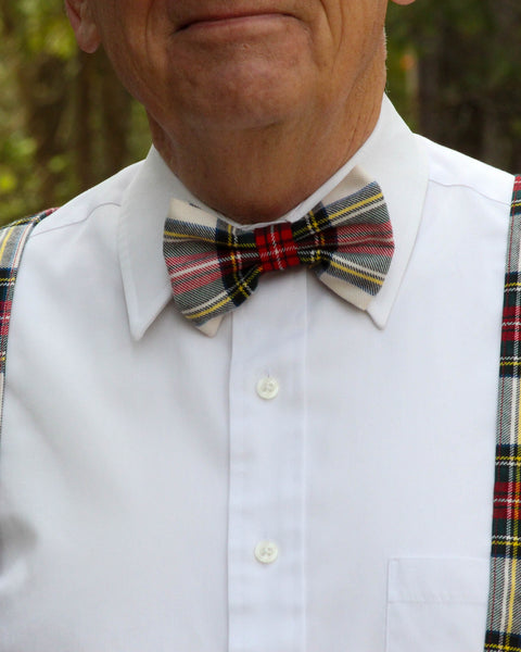 Man wearing a white shirt with a Dress Stewart plaid bow tie and suspenders outdoors.