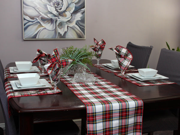 Dining table set with plaid table runner, napkins, and place settings in a room with a floral painting on the wall.
