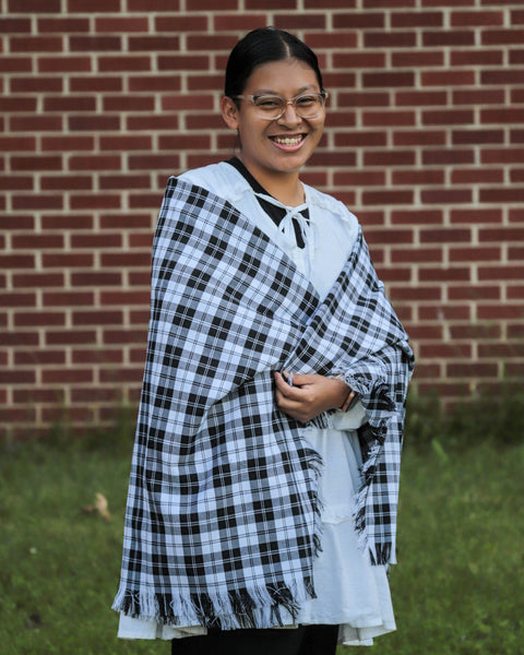 Person wearing a black and white checkered shawl over a light-colored top against a brick wall.