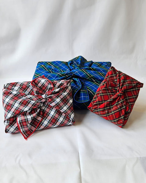 3 packages wrapped in plaid reusable wrapping paper in royal blue, red plaid, white and red plaid