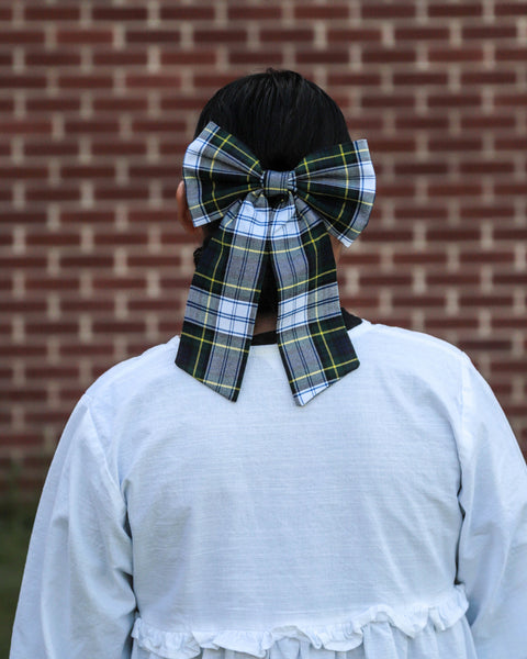woman wearing a large  green and navy plaid bow in her dark hair with a brick wall background Gordon Tartan by Taylors Tartans