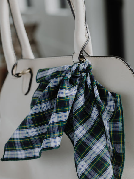 A green, navy, and white plaid cotton scarf knotted and draped over the handle of a white handbag.