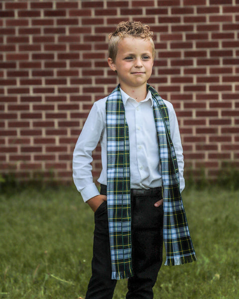 Young boy wearing a plaid scarf in front of a brick wall