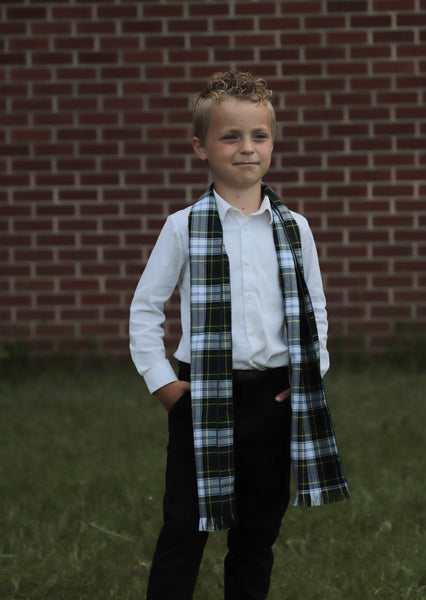 Young boy wearing a  navy and green plaid scarf in front of a brick wall