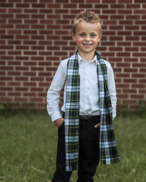 Young boy wearing a plaid scarf in front of a brick wall