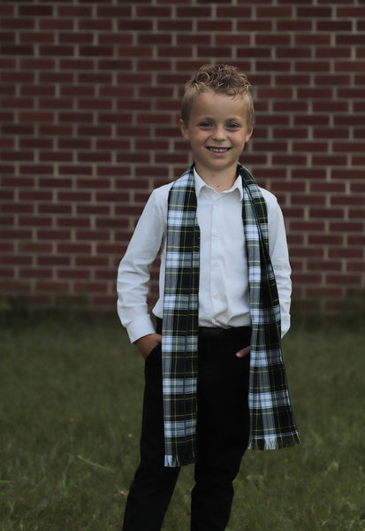 Young boy wearing a plaid scarf in front of a brick wall