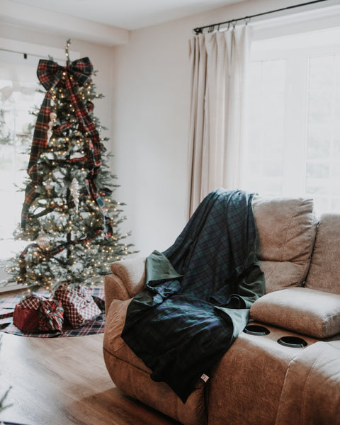 green stewart tartan christmas tree bow with wrapped gifts underneath the tree. a plaid blanket is drapped over a couch in the foreground.