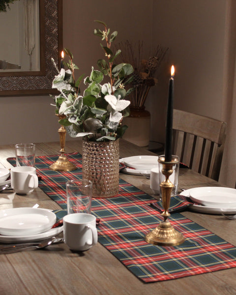 Dining table set with Green Stewart plaid placemats, candles, and a vase with greenery.