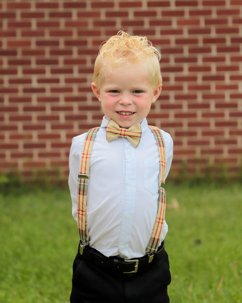 Young boy wearing a Saskatchewan tartan bow tie and suspenders standing in front of a brick wall.