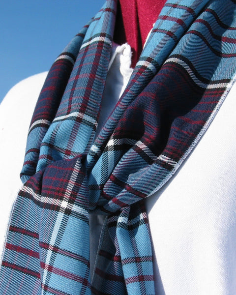 Close-up of a blue plaid scarf with plum and white stripes against a clear blue sky.