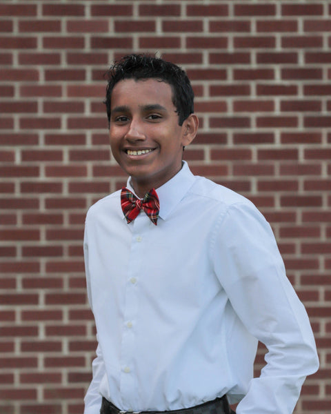 Person wearing a white shirt and Royal Stewart tartan bow tie against a brick wall