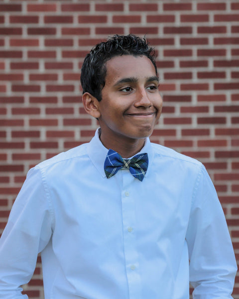 Grinning Person wearing a white shirt and blue bow tie against a brick wall