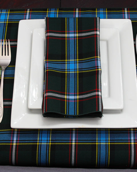 Green blue and white Labrador tartan napkin on a white plate stack with matching table runner underneath.