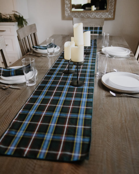 Labrador tartan tablerunner green blue white red and yellow plaid on a wooden table with white candles on holders and white dishes and silverware