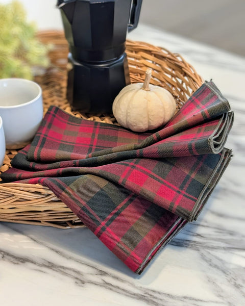 Red green gold Plaid napkins on a marble surface with a coffee maker and small pumpkin in the background.