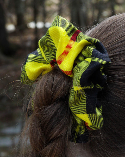 Plaid scrunchie in yellow red and blue on a person's hair with a blurred natural background