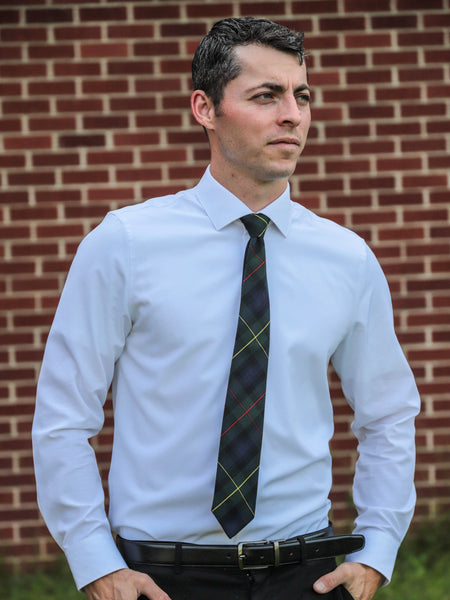 Man wearing a light blue dress shirt and navy and green plaid tie against a brick wall.