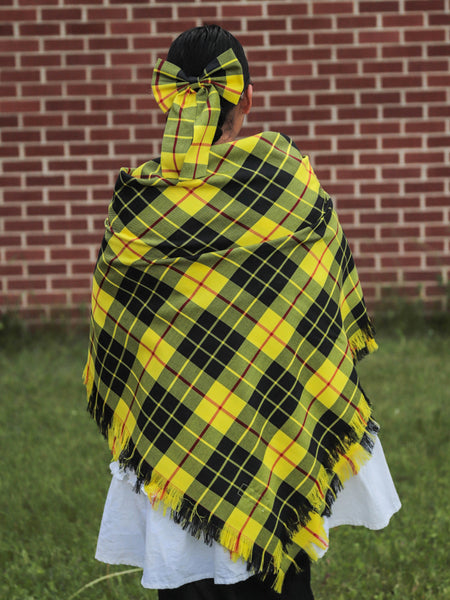 Person wearing a bright yellow and black McLeod of Lewis tartan plaid shawl in front of a brick wall.