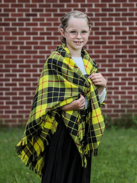 Young girl wearing a yellow and black plaid blanket against a brick wall.