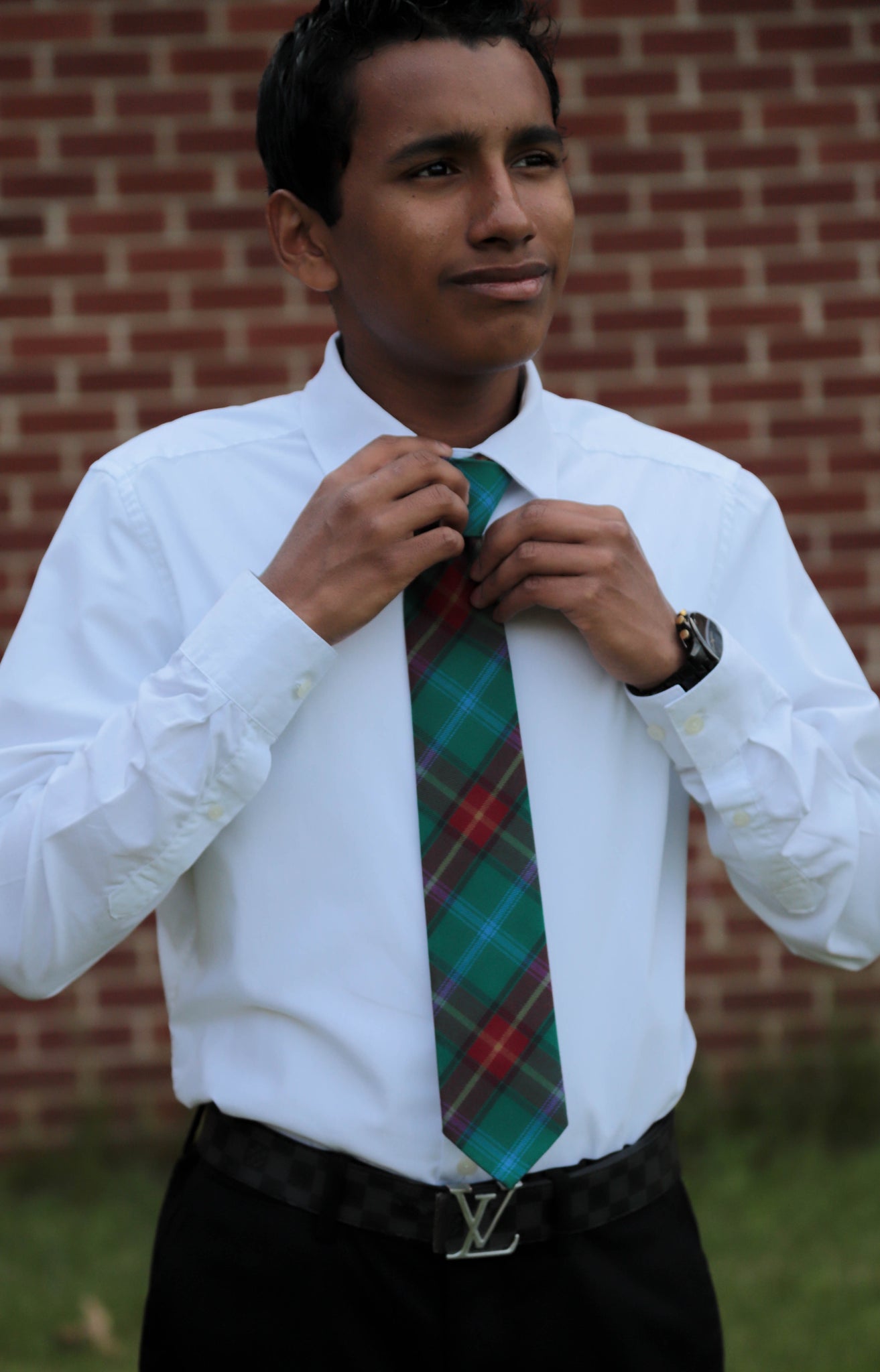 Young man wearing a Manitoba plaid green, red, and white plaid necktie with a white shirt and black pants.
