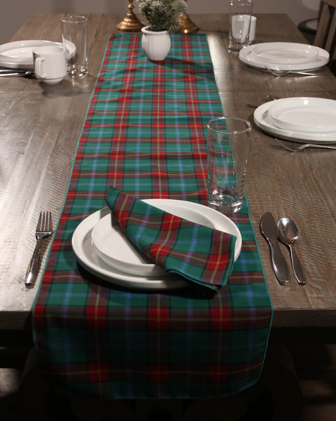 Dining table set with a red green blue and yellow Manitoba tartan plaid napkins matching runner with plates, and cutlery on a wooden surface.