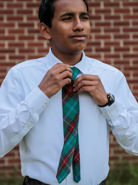 Person adjusting a green plaid tie against a brick wall background