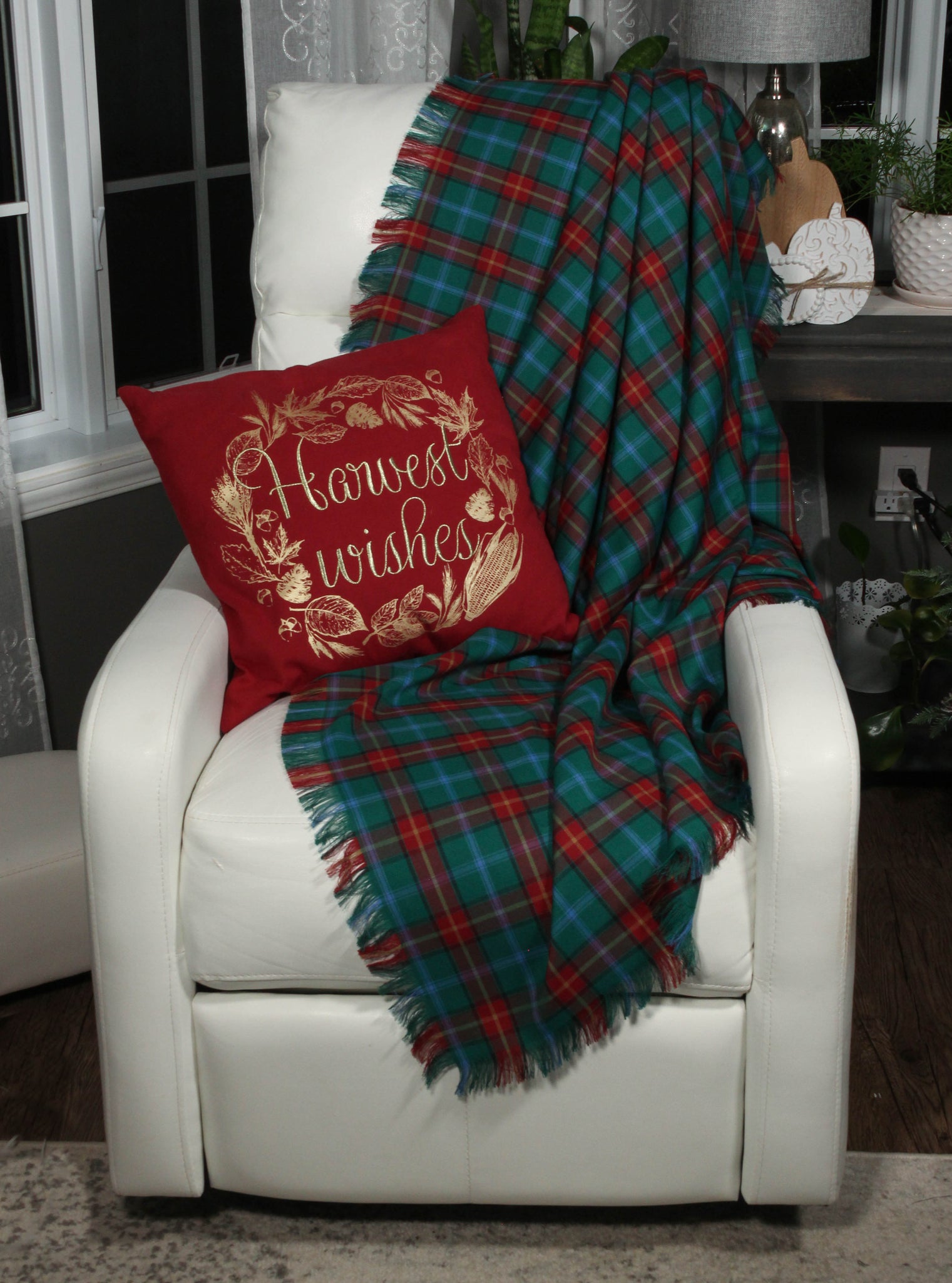 A cozy, teal and red plaid Manitoba tartan throw blanket draped over a white chair, with a decorative red pillow.