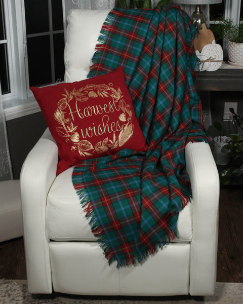 White chair with a red 'Harvest Wishes' pillow and green plaid Manitoba tartan throw in a cozy room.