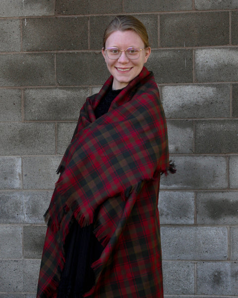 Person wearing a brown and red plaid shawl against a gray brick wall
