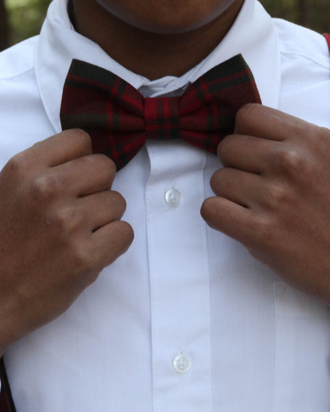 Person adjusting a red green gold and brown plaid bow tie on a white shirt.