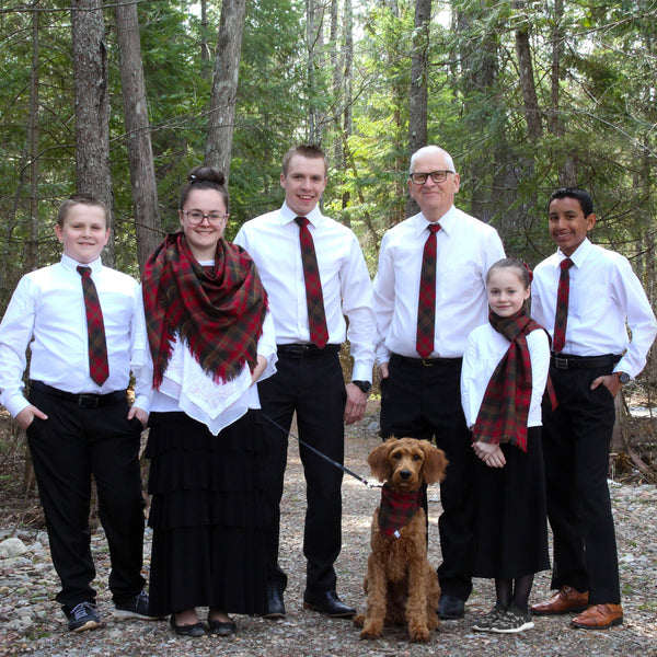 Family of six with a dog in a forest setting, all wearing white shirts and Maple Leaf tartan ties and scarves.