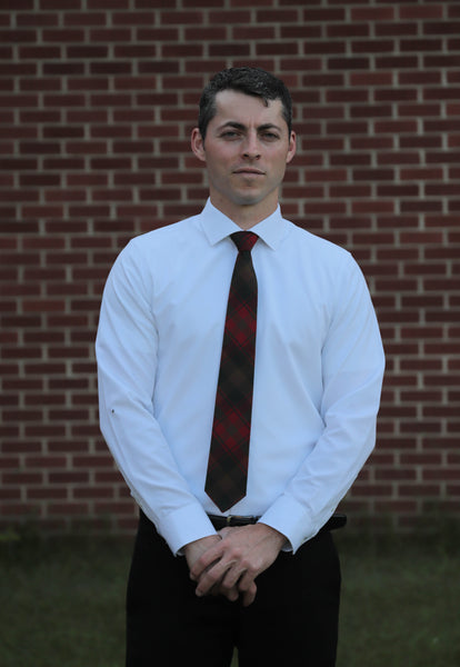Man wearing a white shirt and a Canadian Maple Leaf plaid tie, standing in front of a brick wall.