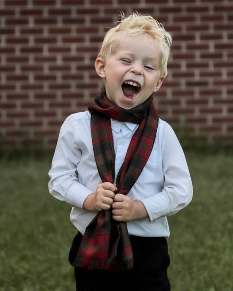 Child wearing a plaid scarf in front of a brick wall
