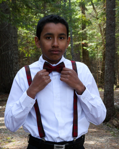 Boy wearing a white shirt, red and brown plaid bow tie, and suspenders made by Taylors Tartans in a forest setting