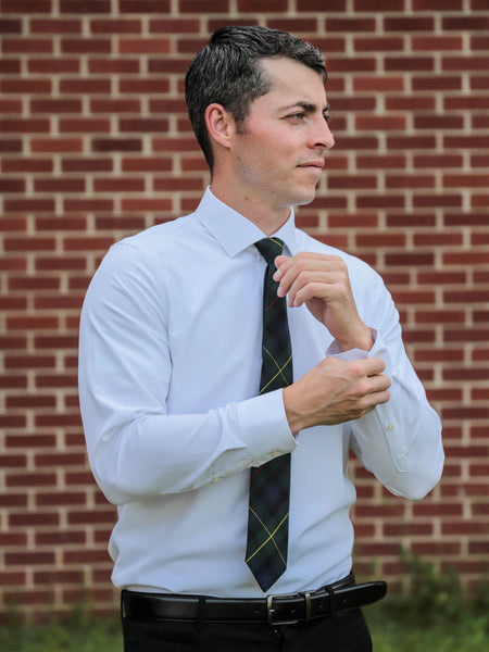 Man adjusting his sleeve wearing white shirt and navy and plaid tie in front of a brick wall