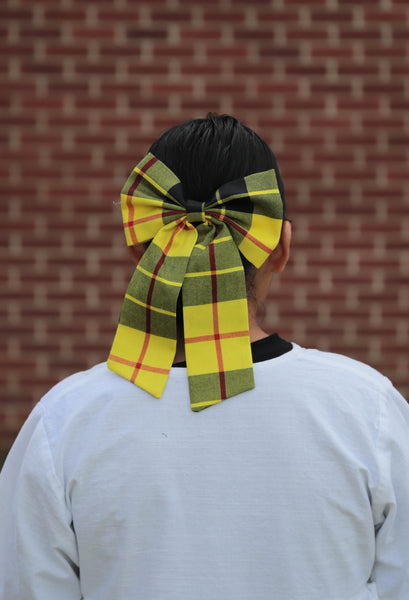 woman wearing yellow and black plaid hair bow, white top, brick wall in background