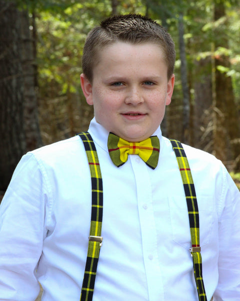 Young boy wearing a white shirt, bright yellow and black plaid bow tie, and suspenders made by Taylors Tartans in a forest setting.