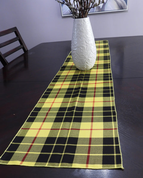yellow and black Plaid table runner on a dark table with a white vase and branches.