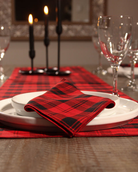 Dining table setting with Menzies red and black plaid napkin, white plates, and wine glasses.