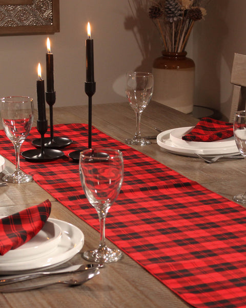 Dining table set with red and black checkered table runner, napkins, black candles, and wine glasses.