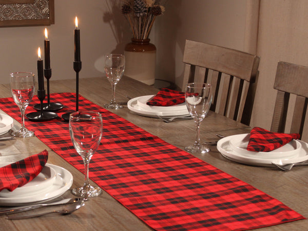 Dining table set with red plaid table runner, black candles, and glassware for formal dinning.