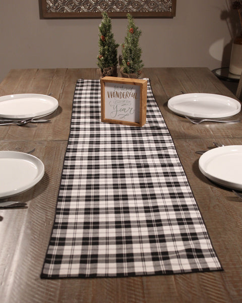 Dining table set with a black and white Menzies plaid runner, framed sign, and small Christmas trees.